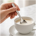Mano revolviendo una taza de café con leche con una cucharita de acero inoxidable