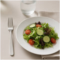 Tenedor de acero inoxidable junto a un plato de ensalada en una mesa servida